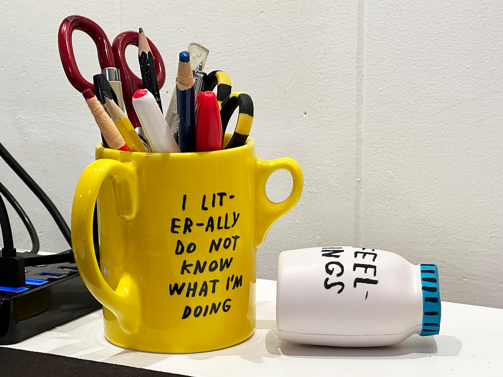 Photo of three handle yellow mug that reads "I LITERALLY DO NOT KNOW WHAT I'M DOING" and jar-shaped stress ball that says FEELINGS. Both by Adam JK.