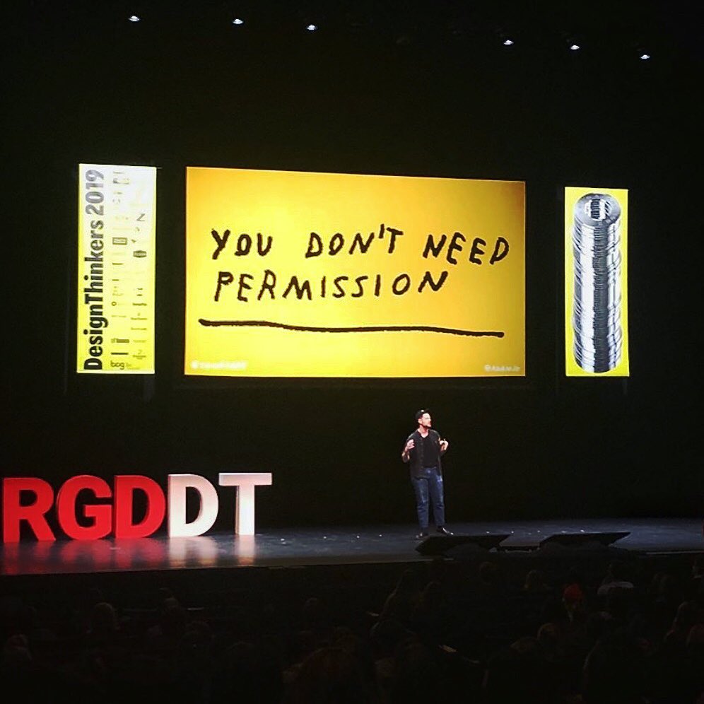 Photo of Adam speaking on conference stage. Slide behind him reads "YOU DON'T NEED PERMISSION" handwritten in large letters on a yellow background.