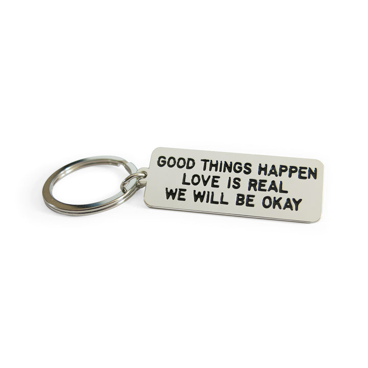 Metal keychain reads GOOD THINGS HAPPEN LOVE IS REAL WE WILL BE OKAY. Art and words by Adam JK.