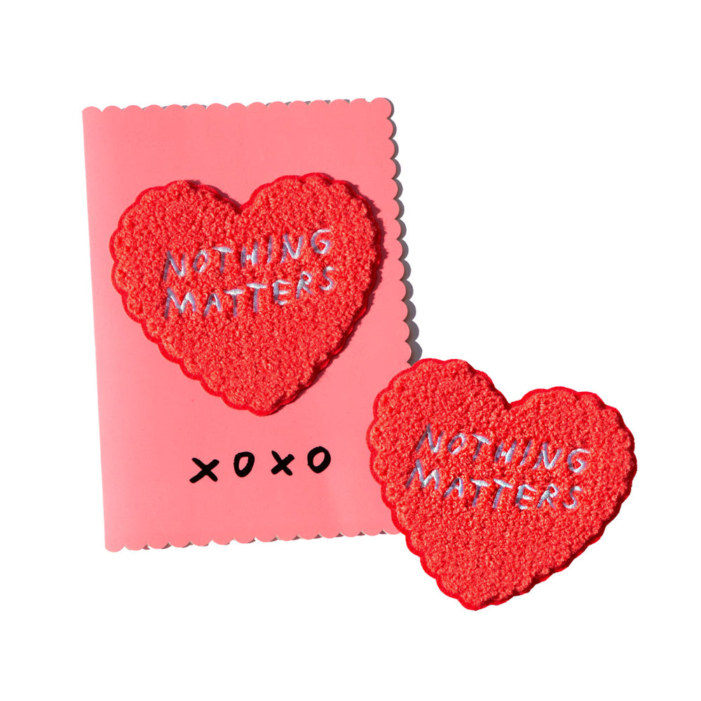 Pink greeting card has removable heart-shaped chenille patch. Patch reads "NOTHING MATTERS" in handwritten text. By Adam JK.