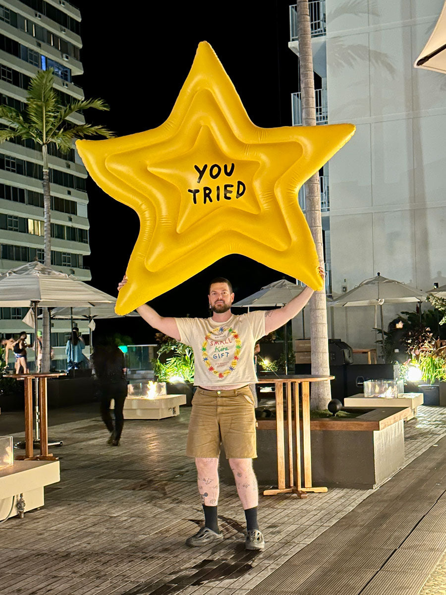 Person holding a large inflatable star with 'YOU TRIED' text in an outdoor setting.